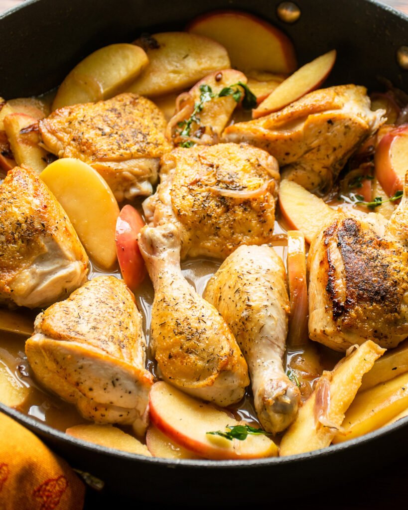 Chicken, apples and onions cooking in a large skillet.