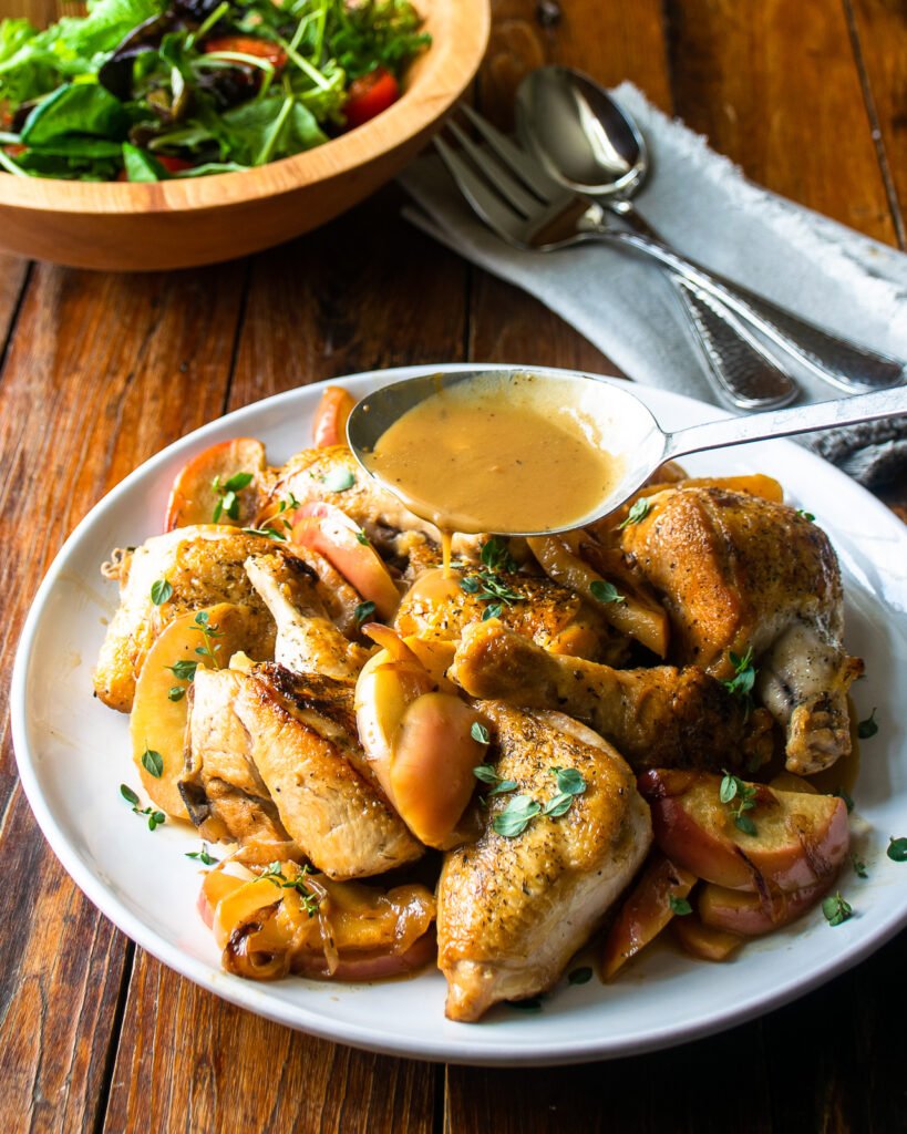 Apple Cider Glazed Chicken on a white plate with a bowl of salad and serving utensils.