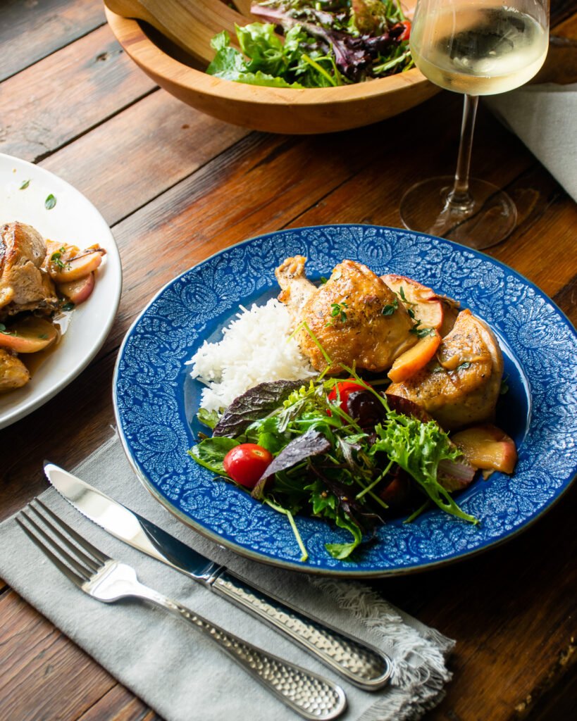 Cider Glazed Chicken on a blue plate with rice and a side salad, on a wooden table with more chicken and a bowl of salad next to it.