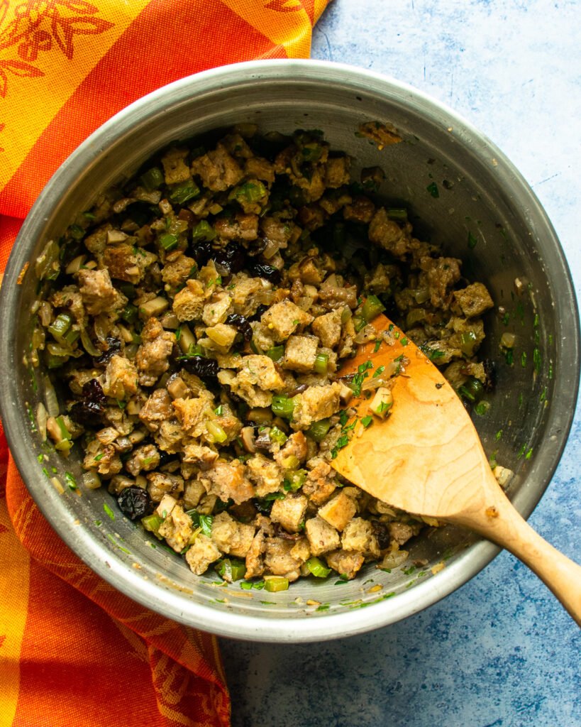 Sausage and breadcrumb stuffing in a bowl with a wooden spoon and an orange towel.
