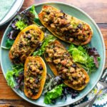 Stuffed Delicata Squash on a green platter with salad greens on a wooden table with servers.