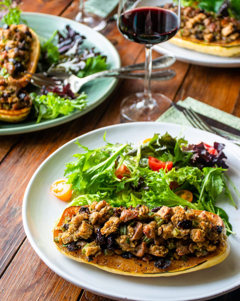 A white plate with half a stuffed delicata squash, a side salad, a glass of red wine.