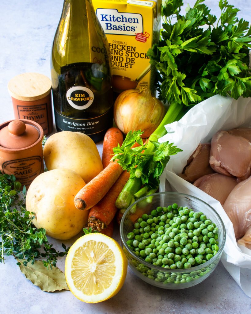 Ingredients on a counter - raw chicken, frozen peas, lemon, carrots, celery, onion, potatoes, white wine, stock, and some herbs and spices.