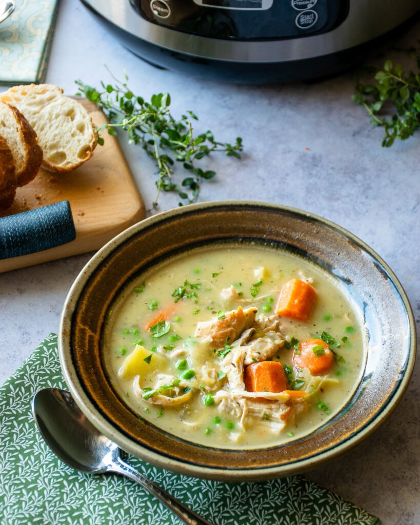 Instant chicken stew in a brown ceramic bowl with a green napkin and spoon next to it and some sliced baguette near by.