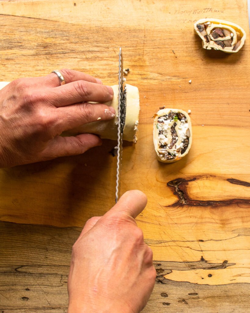 Hands slicing a log of stuffed puff pastry.