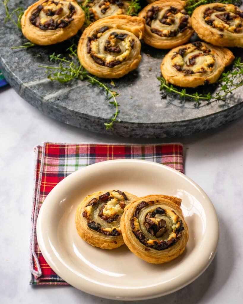 Two pinwheel pastries on a white plate with a platter behind them.