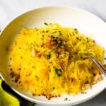 Spaghetti Squash with Parmesan-Parsley breadcrumbs on a white plate with green napkin.