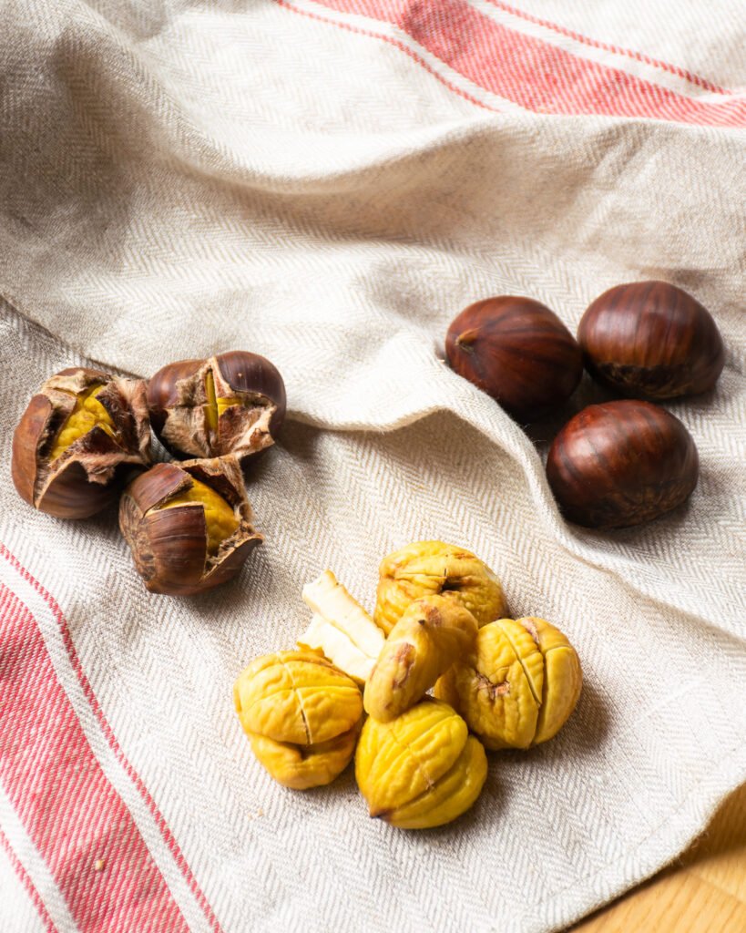 Raw, roasted and peeled chestnuts on a kitchen towel.