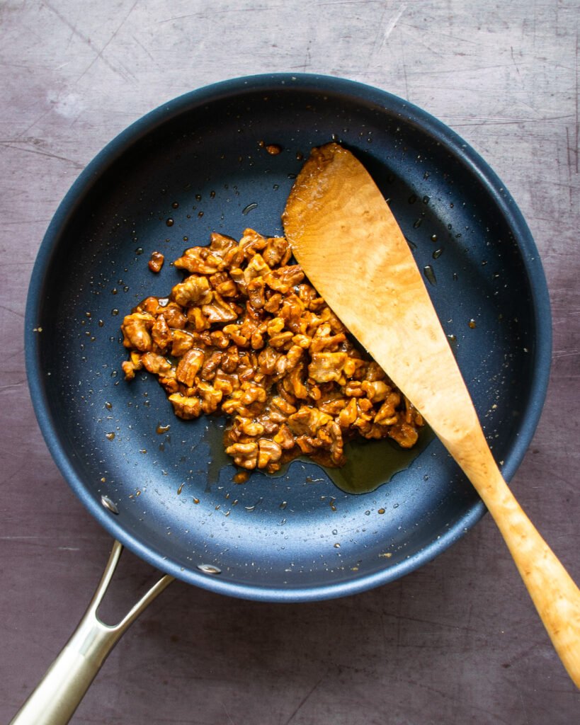 Candied walnuts and a wooden spoon in a blue non-stick skillet.