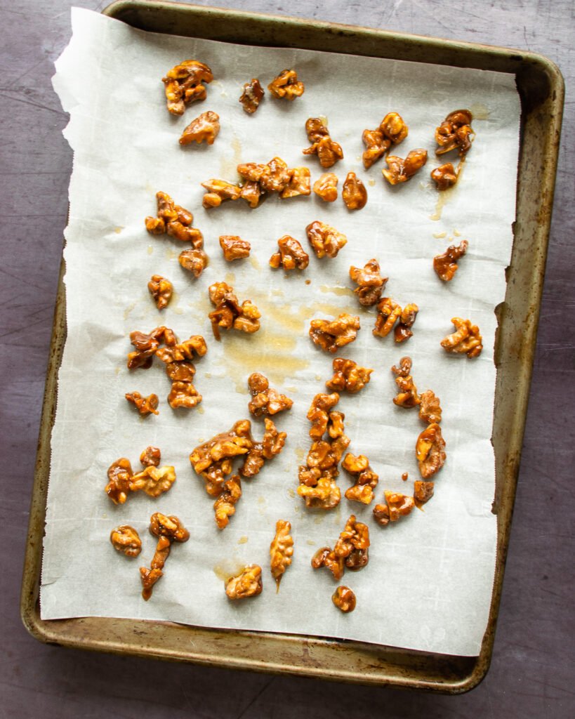 Candied nuts on parchment paper on a baking sheet.