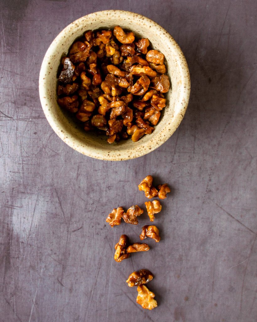 Candied nuts in a ceramic dish with some on the countertop.