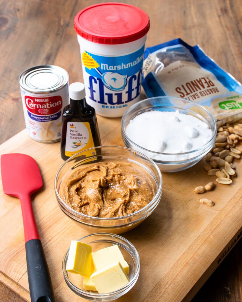 Ingredients on a cutting board - marshmallow creme, sugar, evaporated milk, vanilla, peanut butter, butter and roasted peanuts.