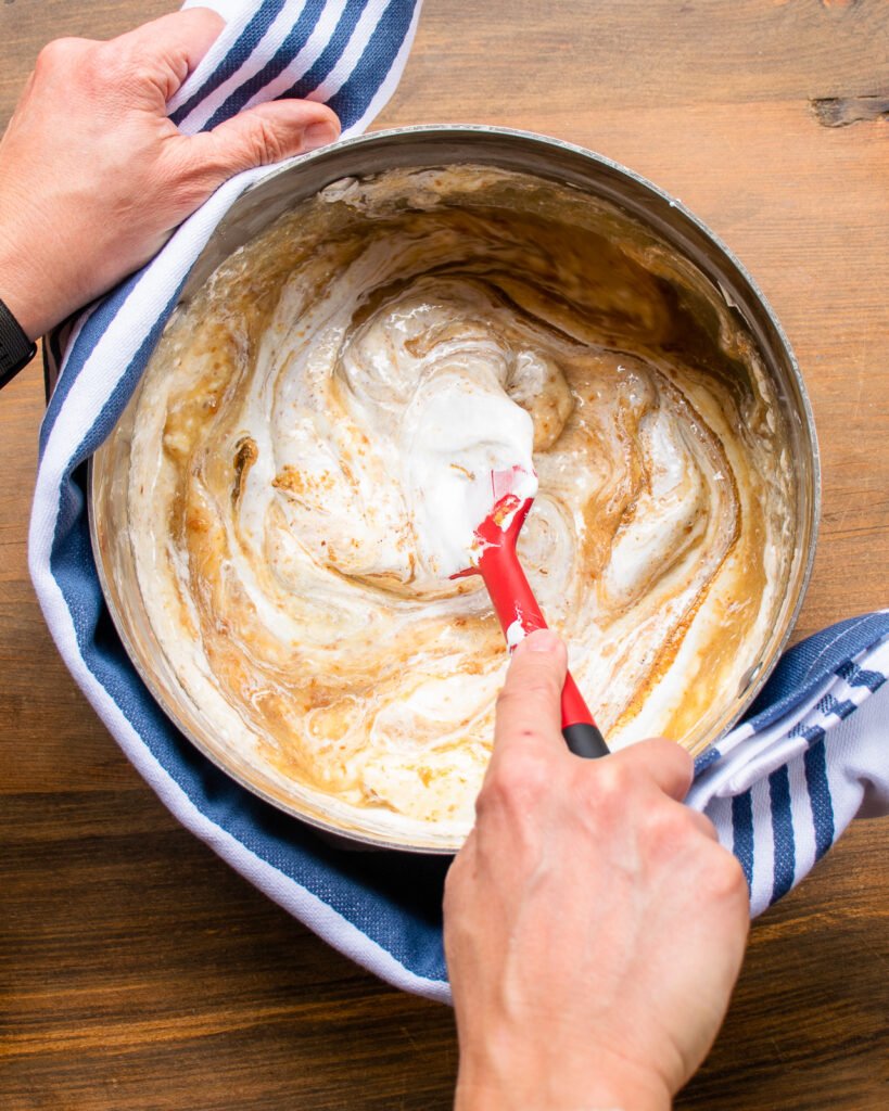 Hands stirring ingredients together in a large saucepan.