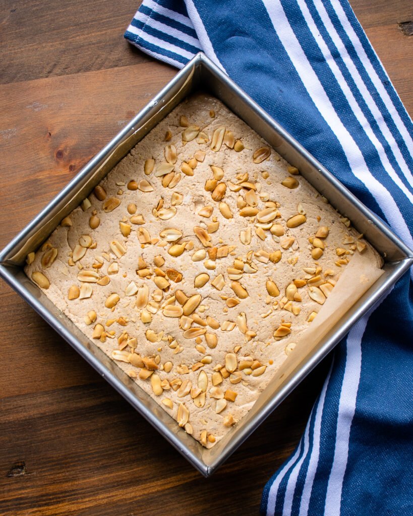 Peanut butter fudge in a square cake pan with a blue and white towel next to it.