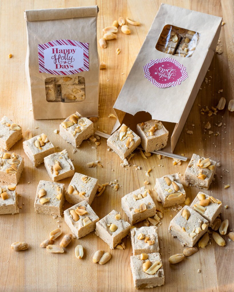 Peanut butter fudge squares on a cutting board with paper bags of fudge wrapped for the holidays in the background.