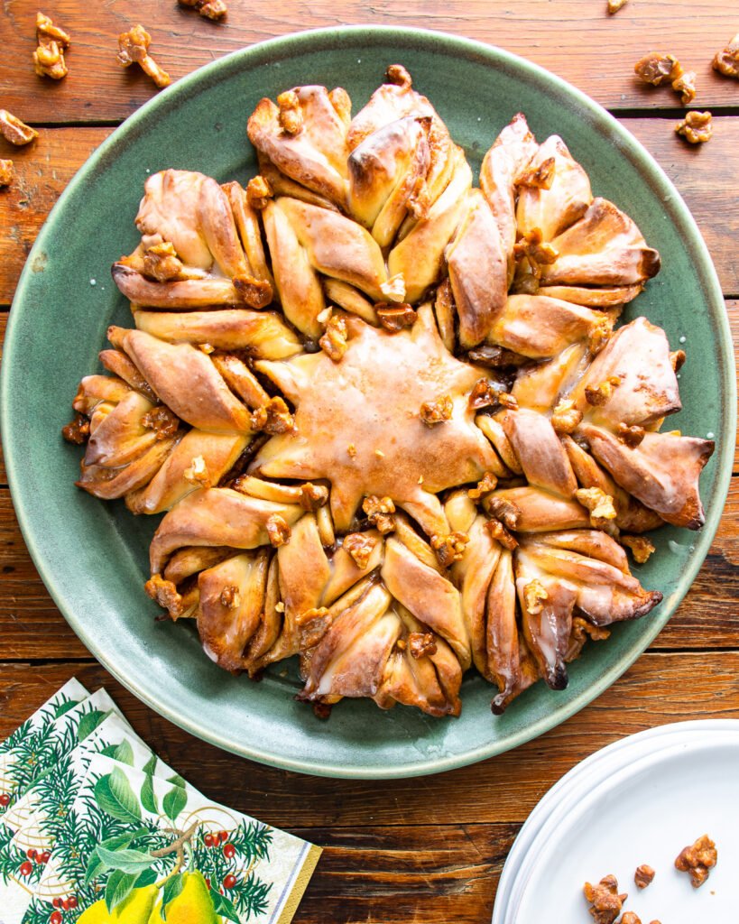 Star bread with candied walnuts on a green platter with holiday beverage napkins and a stack of white plates.