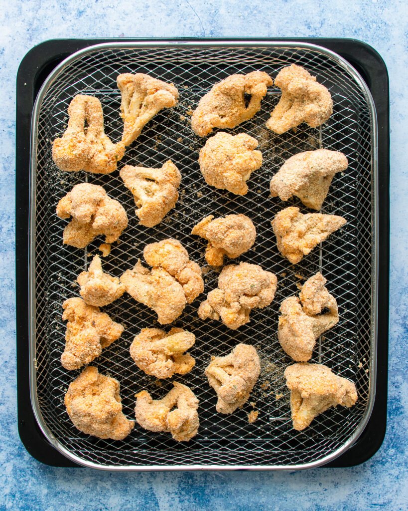 Breaded buffalo cauliflower florets on an air fryer rack.