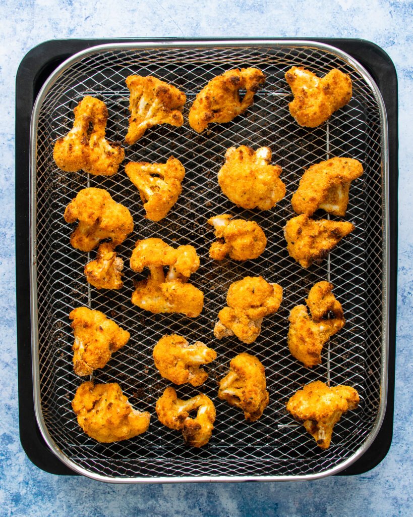 Cooked Buffalo cauliflower florets on an air fryer rack.