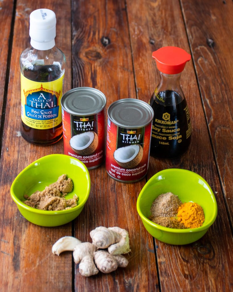 Ingredients on a table - coconut milk, fish sauce, soy sauce, brown sugar, spices, ginger and garlic.