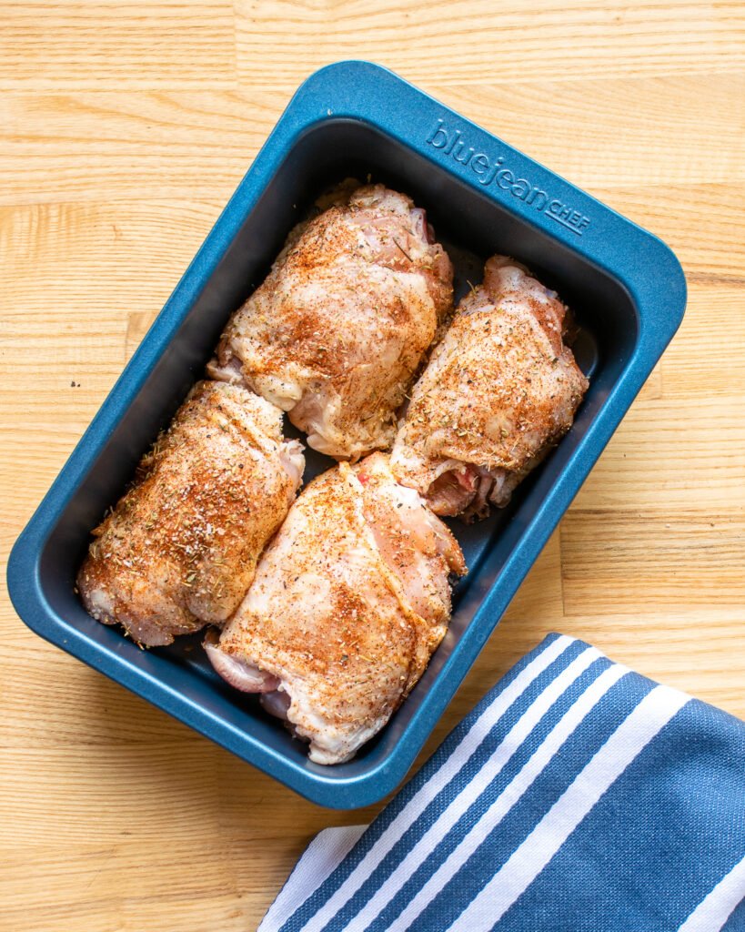 Four chicken thighs in a blue baking pan.