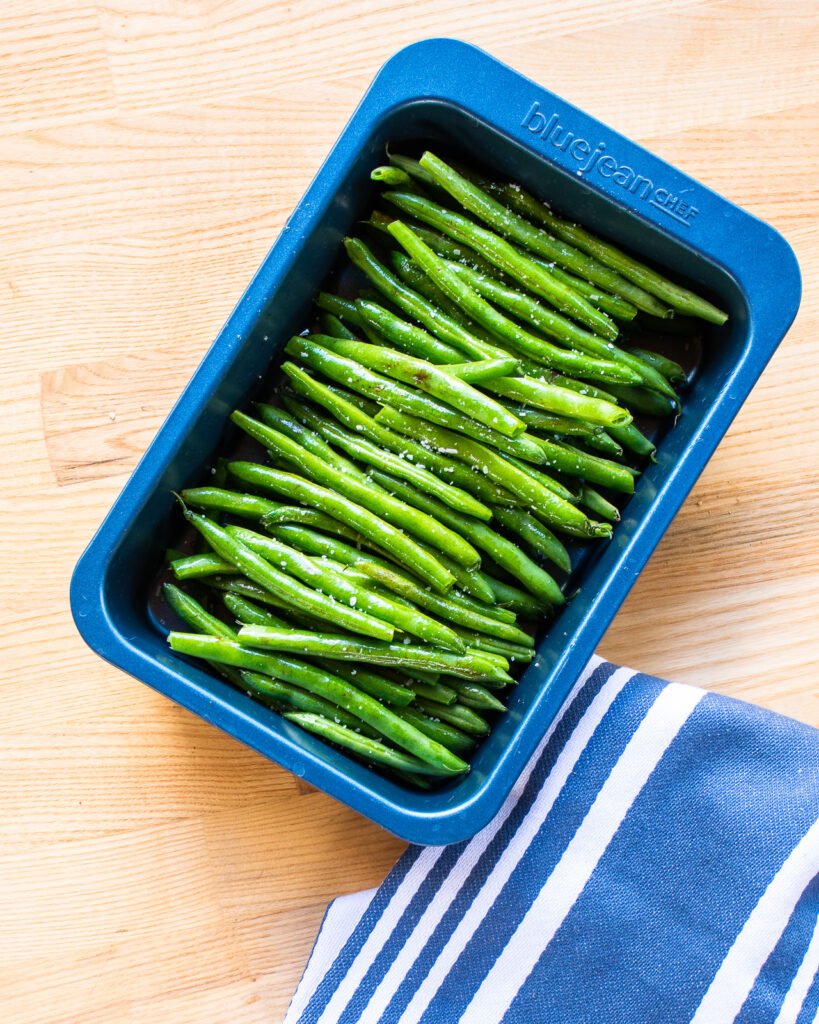 Green beans in a blue baking pan with a blue and white striped towel.