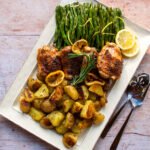 Honey Baked Chicken with crispy potatoes and roasted green beans on a rectangular platter with serving utensils.