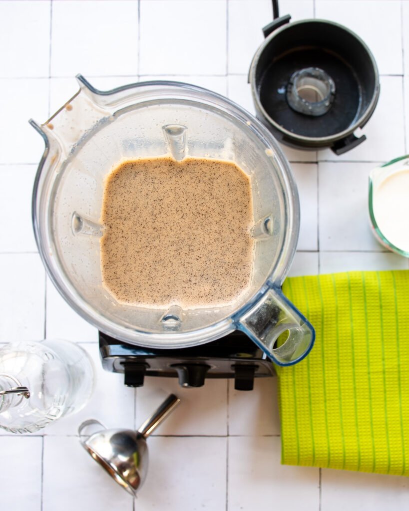 Looking down into a blender with homemade Irish cream inside and a green towel next to it.