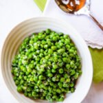Minted peas in a ribbed white bowl with a serving spoon and green and white napkins.