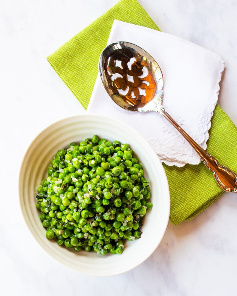 Minted peas in a ribbed white bowl with a serving spoon and green and white napkins.