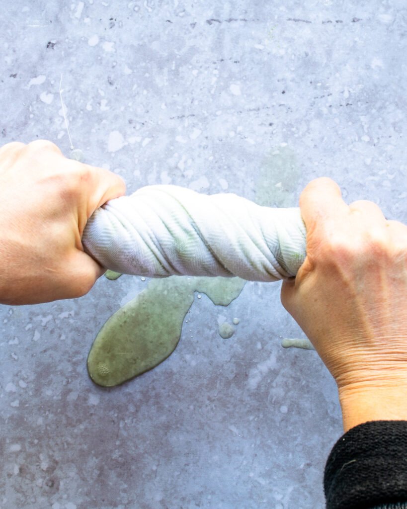 Hands wringing a cloth over a countertop with a green water dripping out.