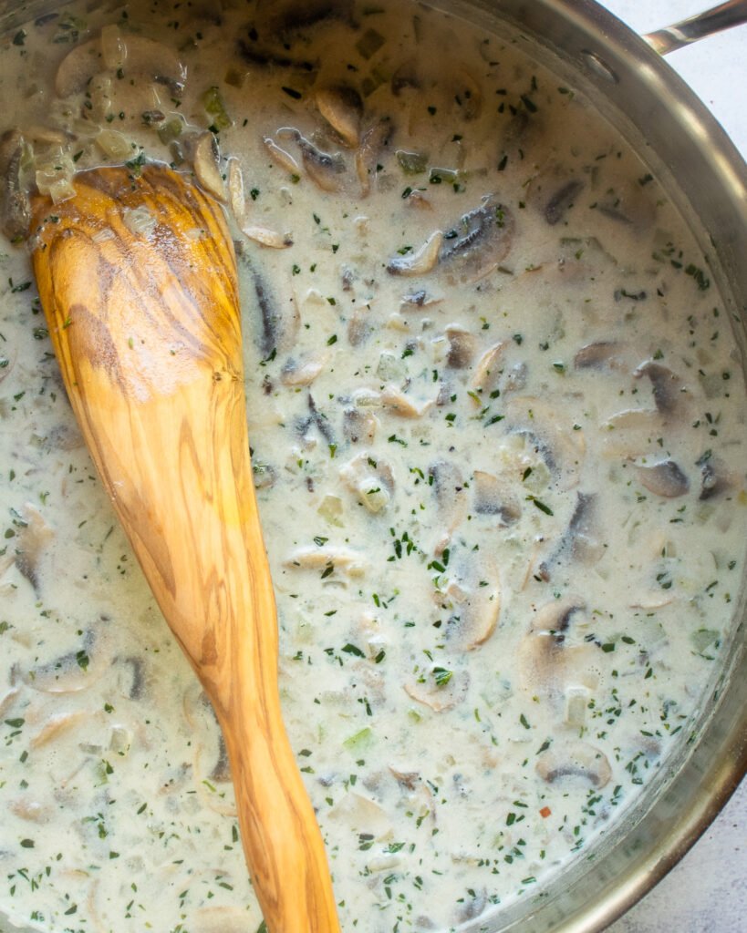 The sauce for tuna noodle casserole in a saute pan with a wooden spoon.