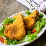 Two air fryer breaded pork chops on a lettuce lined oval white plate on a rustic wooden table.