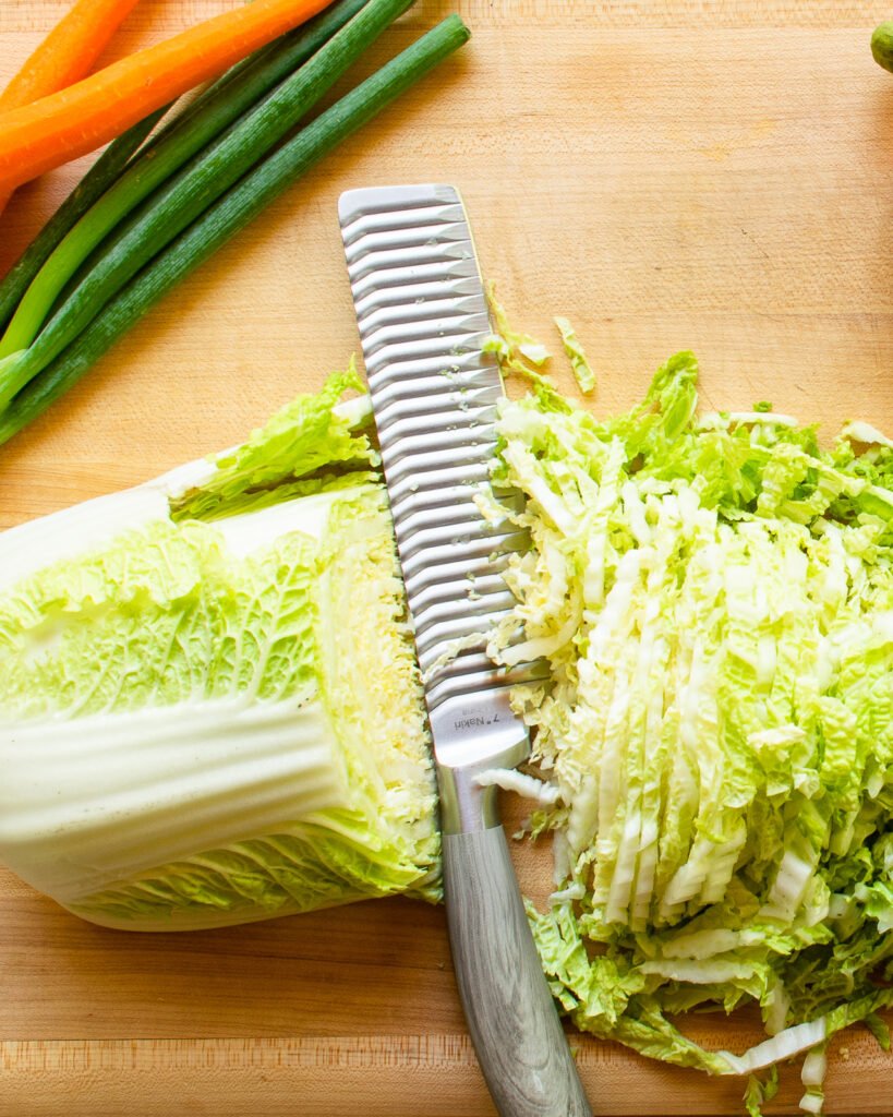 A nakiri knife cutting napa cabbage into thin slices.
