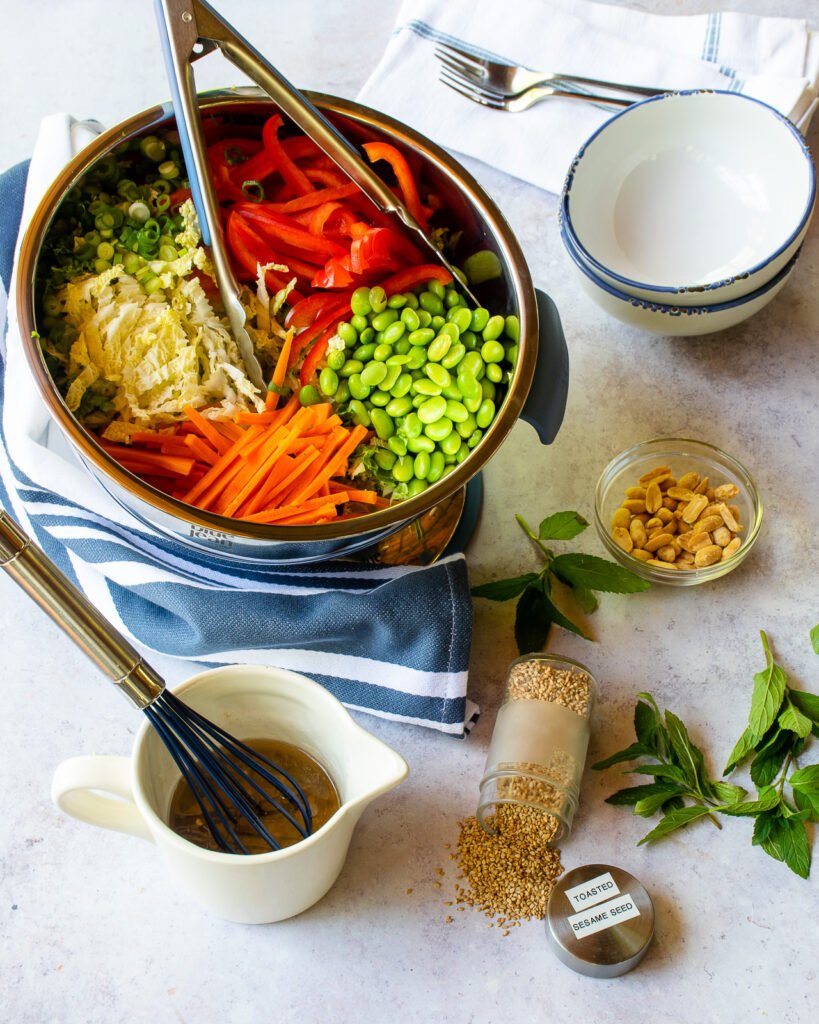 A ceramic measuring cup of ginger sesame dressing with a bowl of Asian slaw in the background.