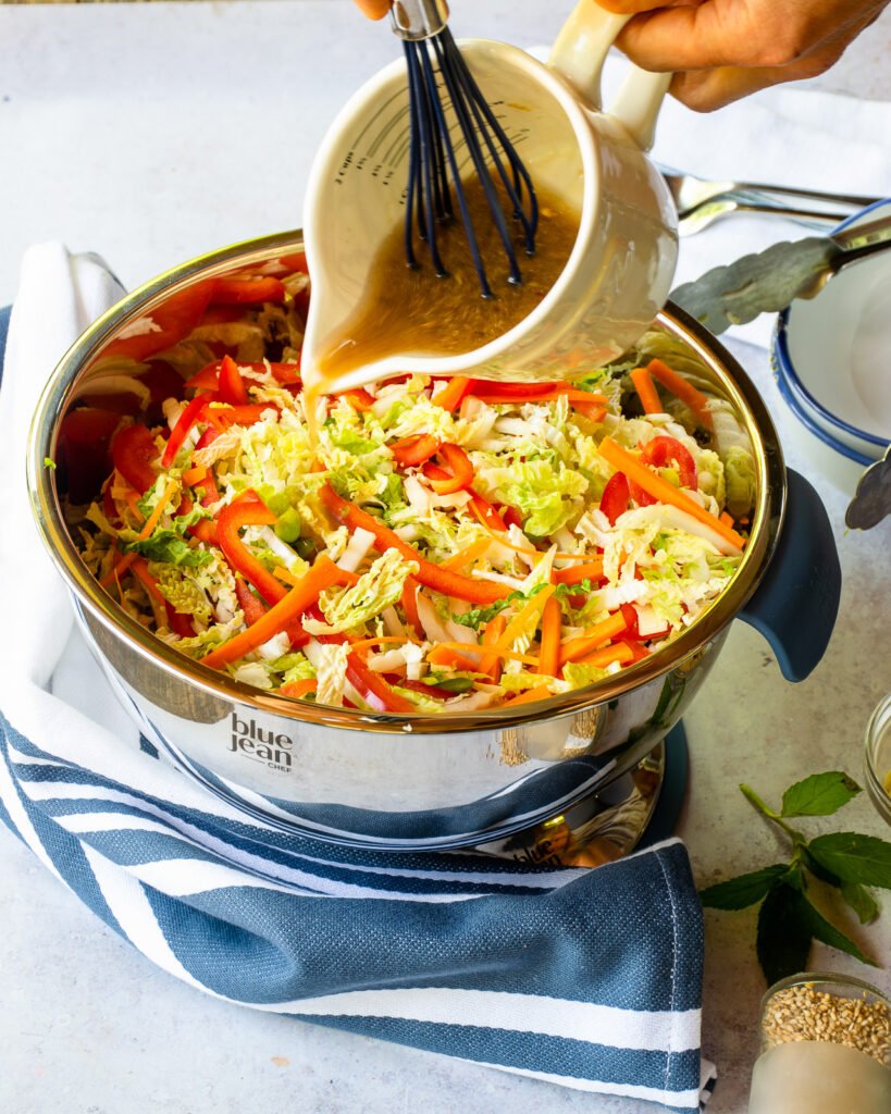 Pouring a dressing over a bowl of Asian slaw.