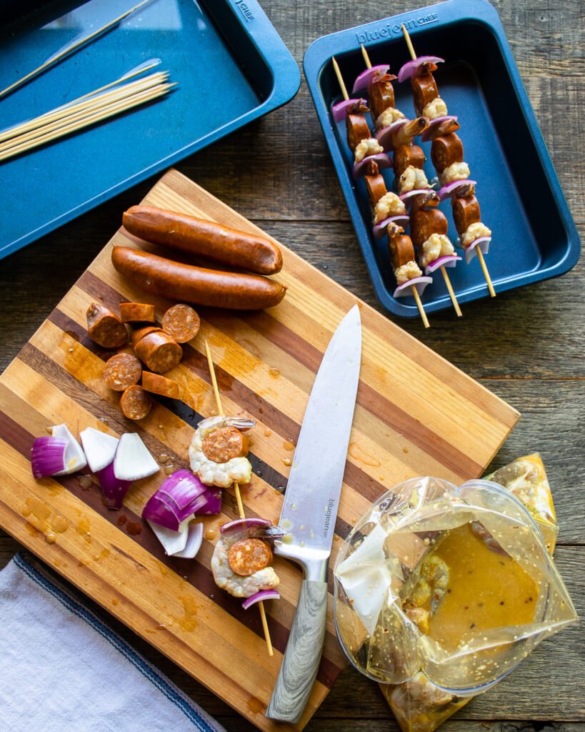 Shrimp and chorizo pieces being skewered on a wooden cutting board.