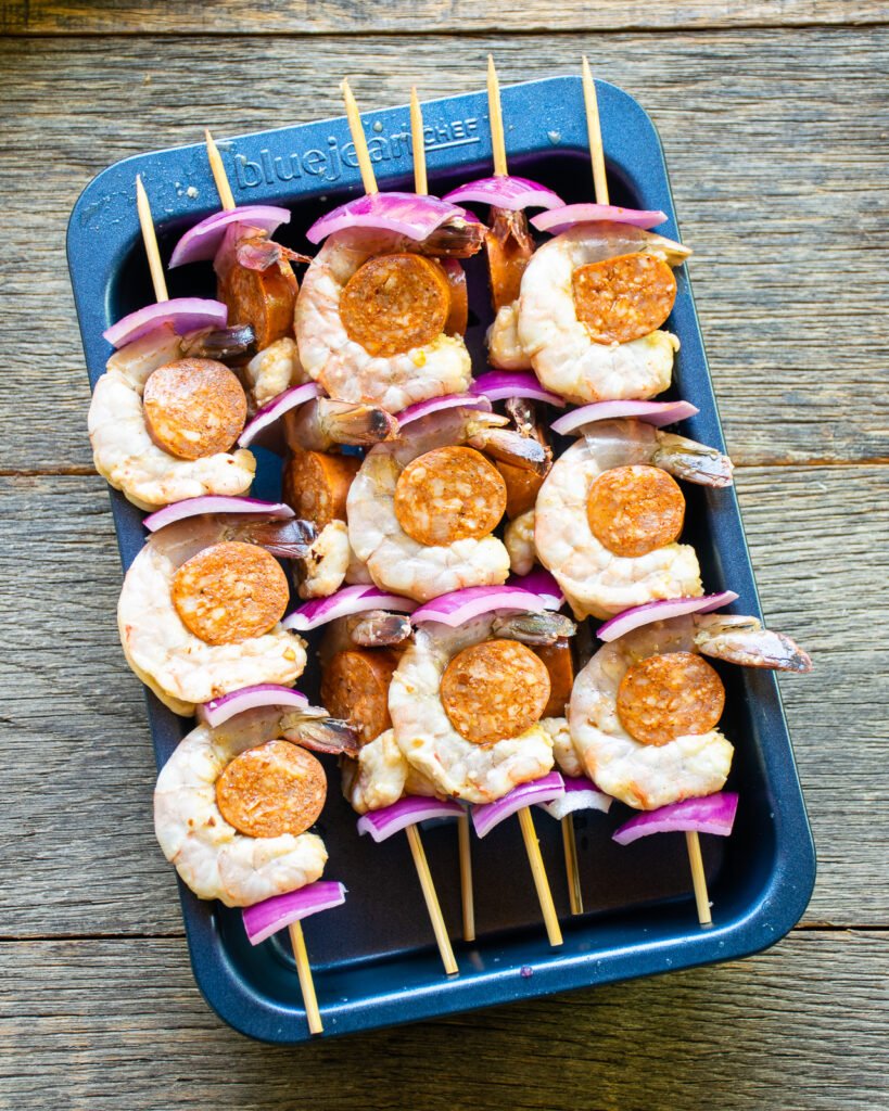 Skewered shrimp and chorizo resting in a blue baking pan.