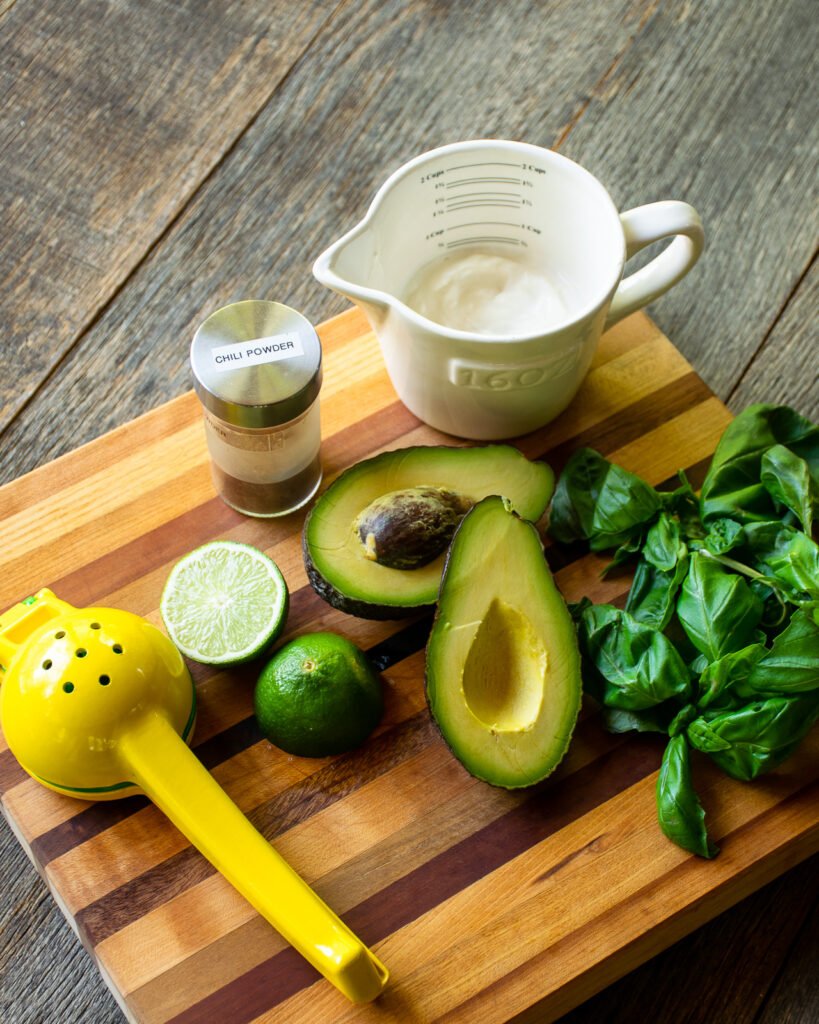 Ingredients on a cutting board - yogurt, avocado, basil, lime and chili powder.