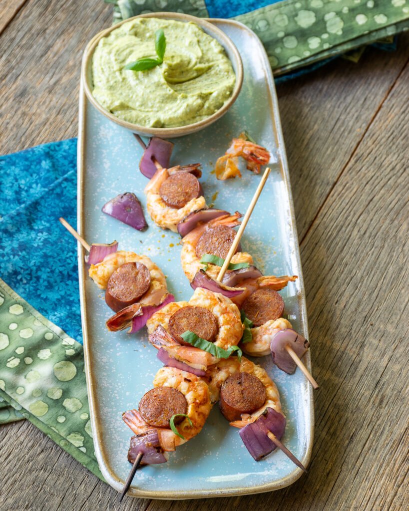 Shrimp chorizo skewers on a blue rectangular plate with a green dip.