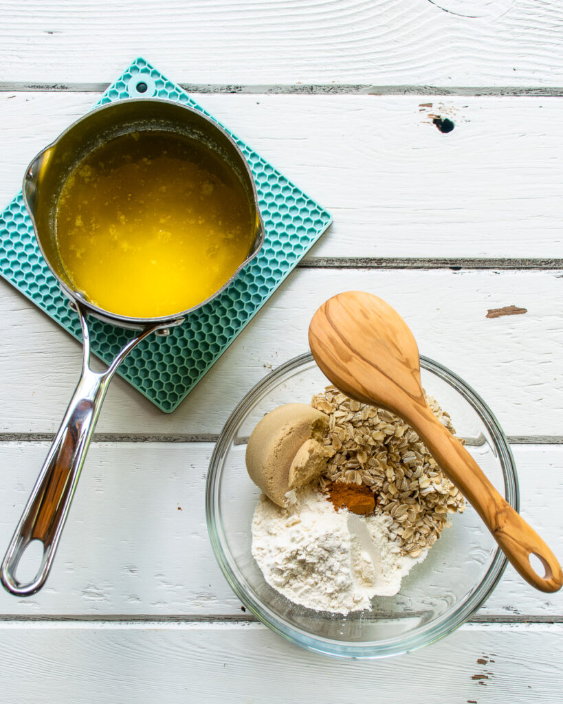 A saucepan with butter and a bowl with ingredients and a wooden spoon on a white wooden table.