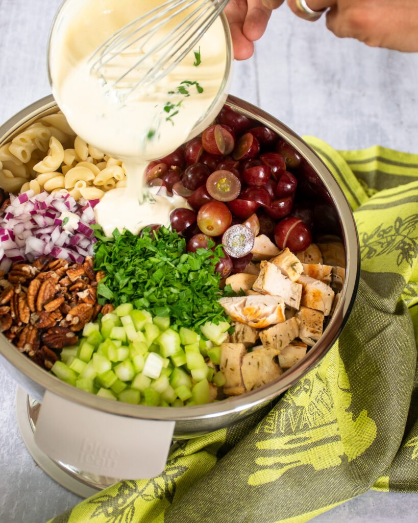 Ingredients for chicken macaroni salad in a bowl with dressing being poured on top.