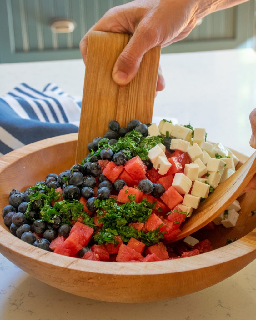 Hands tossing a salad in a wooden bowl.