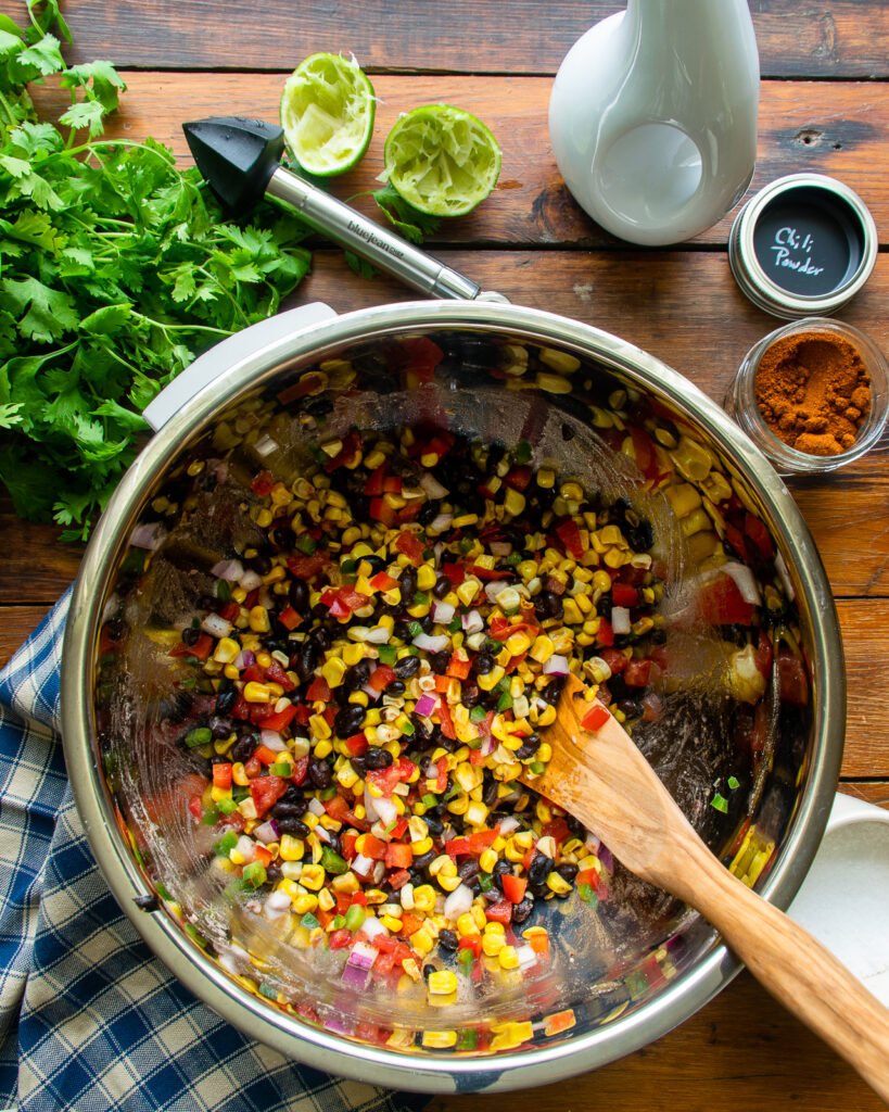 Corn and black bean salsa mixed in a bowl with a wooden spoon.