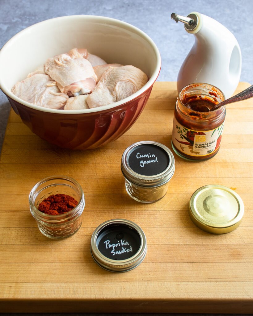 Ingredients on a cutting board - cut up chicken, olive oil, harissa and spices.