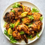 Grilled Harissa Chicken on a white plate with lemon slices and greens.