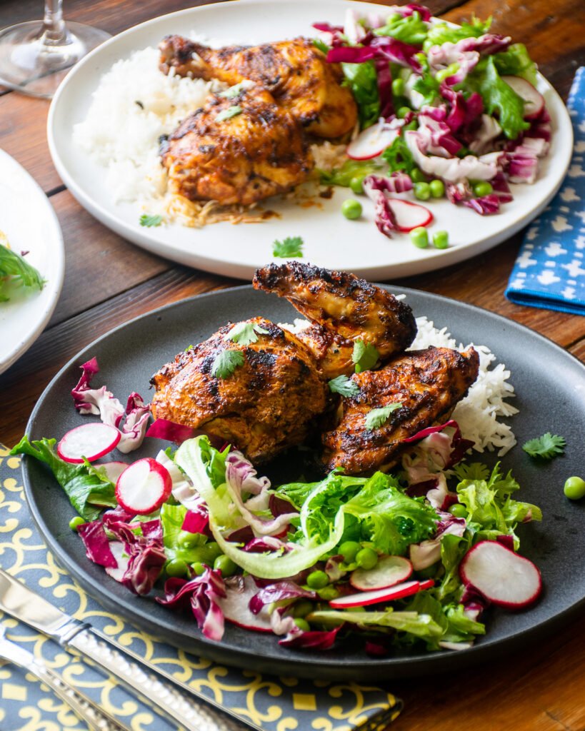 A gray dinner plate on a wooden table with grilled harissa chicken, rice and salad.