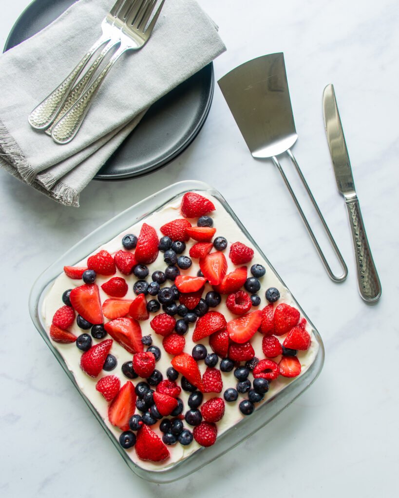 Looking straight down on mixed berry tiramisu with a stack of plates, napkins and forks near by.