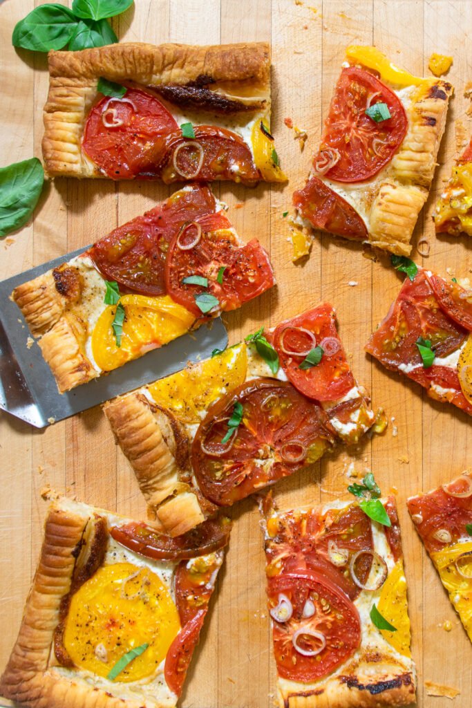 Tomato Tart cut into squares on a wooden cutting board.