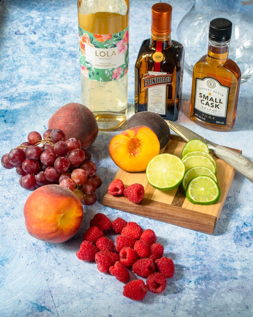 Ingredients for sangria on a blue countertop - fruit, wine and liquor.