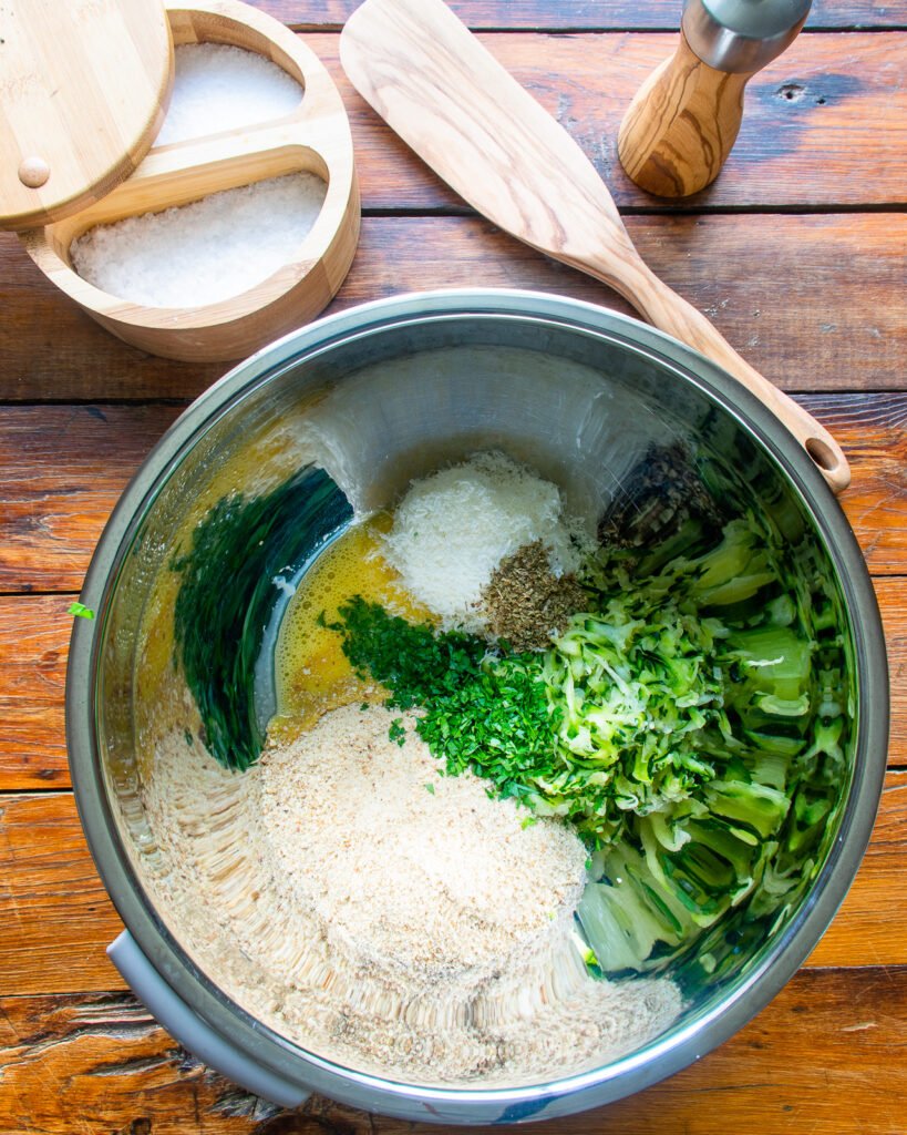 ingredients in a stainless steel bowl with salt, a wooden spoon and a wooden peppermill on a wooden table.